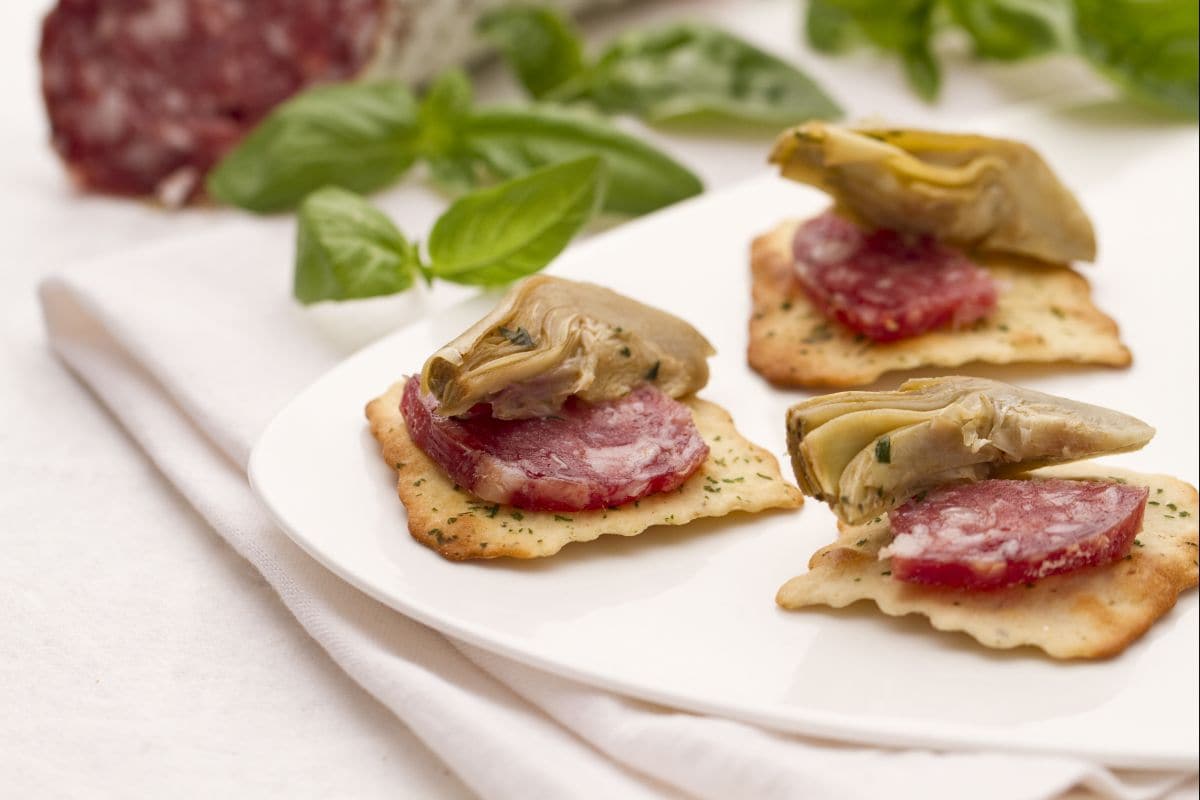 Artischocken und Salami auf Olivencrackern